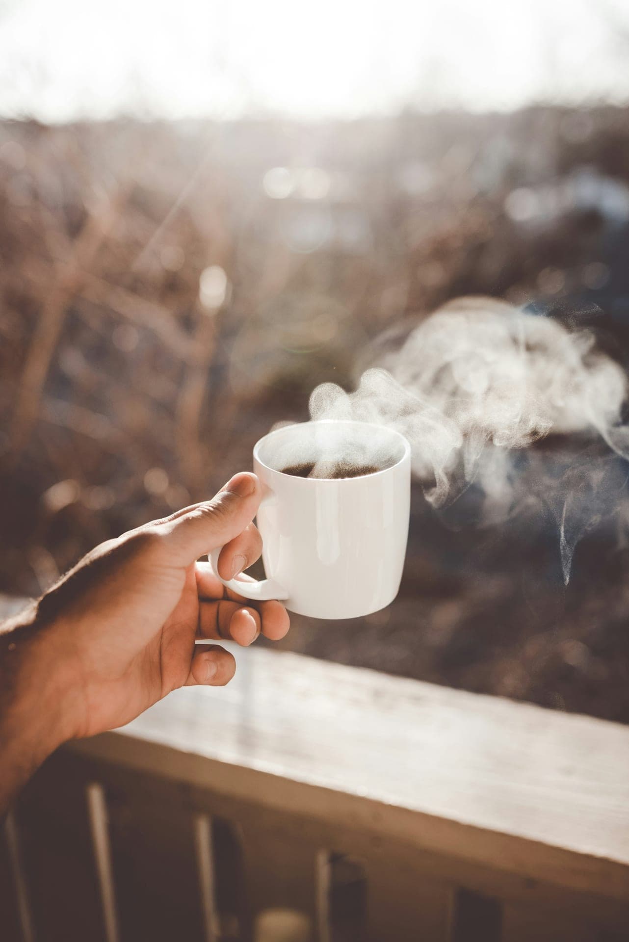 Hand holding a steaming mug outdoors in sunlight