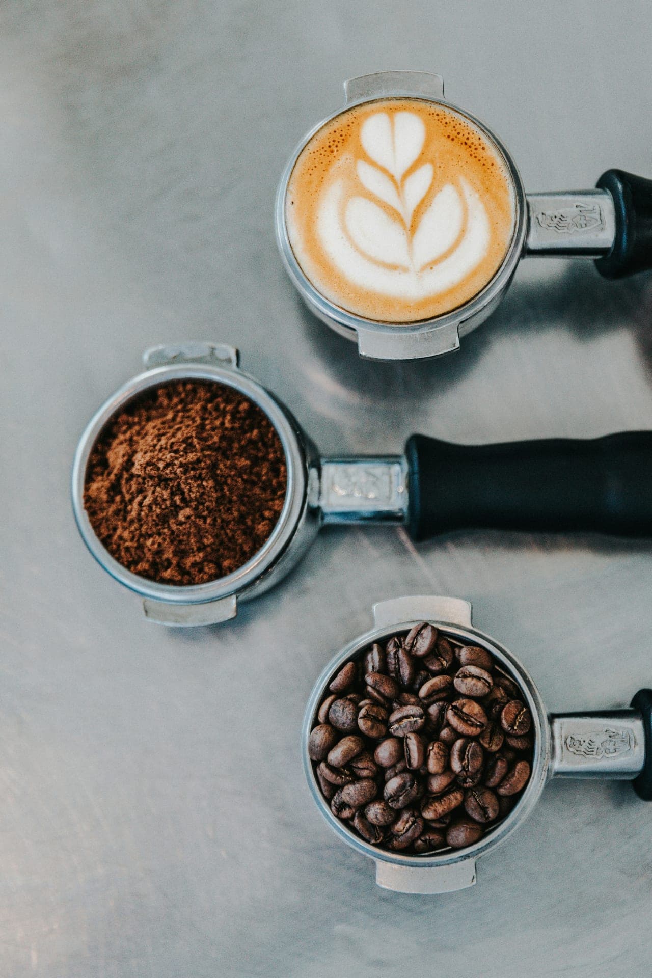Three portafilters with beans, grounds and latte